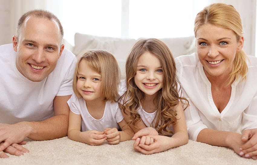 The image depicts a professional rubbish removal scene in a residential area, with a large, white Hire Man and Van van parked on a paved driveway. The van features a sliding side door that is partially open, revealing a glimpse of the cargo space. In the foreground, a substantial heap of mixed household waste is visible, including black bin bags, flattened cardboard boxes, and discarded plastic containers, all arranged in a somewhat organized manner to facilitate loading. The waste is situated close to the rear of the van, which is positioned parallel to a stone-flagged pathway. The driveway is bordered by a low brick wall and a front lawn with neatly trimmed grass, suggesting a suburban neighbourhood, possibly in Ellesmere Port. The background includes the façade of a residential property with brick walls and a tiled roof, and a few garden plants and shrubs are visible along the edges. The lighting indicates an overcast day, with soft, diffuse daylight casting minimal shadows, emphasizing the neutral and quiet atmosphere typical of rubbish collection operations. This scene illustrates a typical local rubbish clearance process handled by Hire Man and Van in the CH66 postcode area, prepared for waste disposal or recycling.